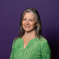 Amy smiling at the camera with a green shirt on and a purple background