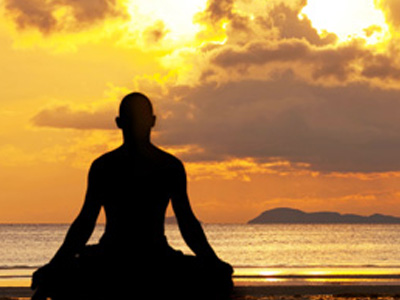 A man meditating on a beach at sunset