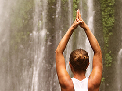 A woman holding a yoga pose in front of a tall waterfall