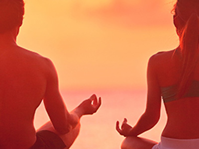 A man and woman meditating on a beach at sunset