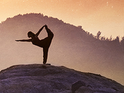 A woman holding a yoga pose on a large boulder, with mountains in the distance