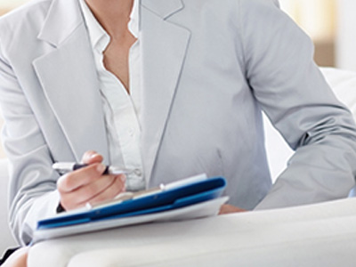 Closeup of a woman wearing business attire who is holding a pen and clipboard