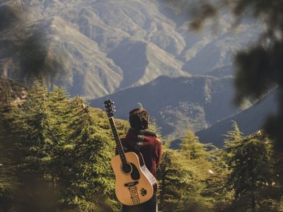 person with guitar facing a scenic mountain overlook