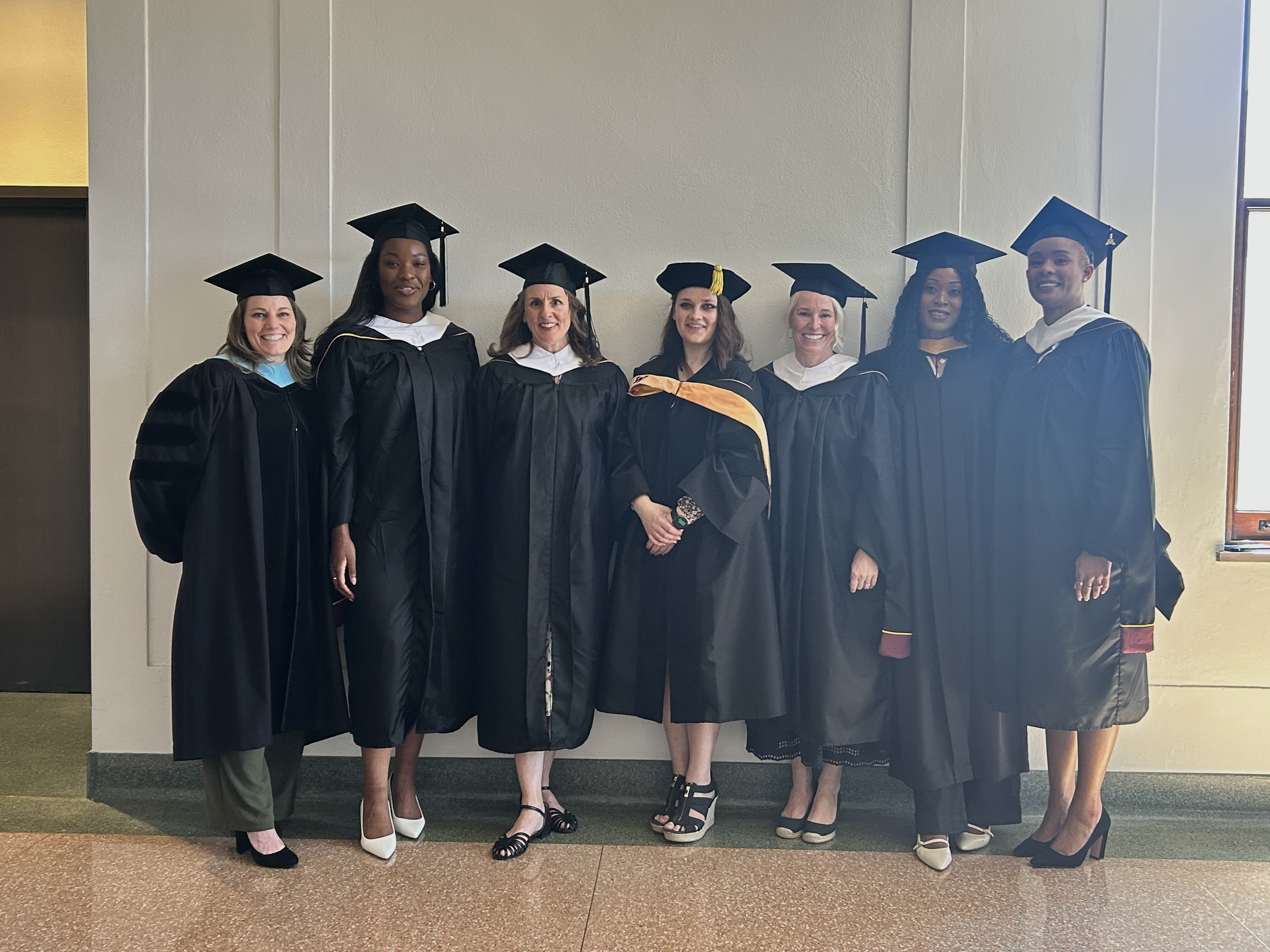 Bakken Center Graduates standing against a white wall in their black graduation gowns
