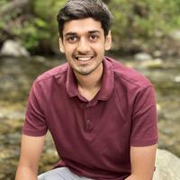 Jaidev sitting on a rock, in a red polo, smiling at the camera