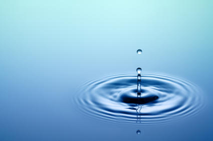 Close-up of a drop of water hitting the surface of a calm body of water.