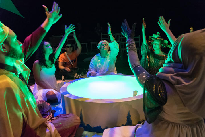 people in costume around a light well extending their hands upwards