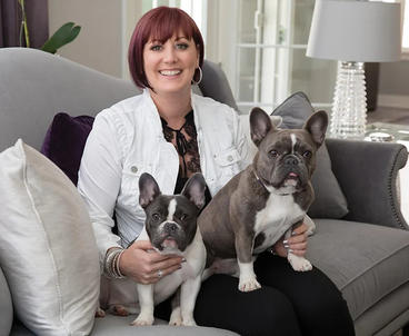 Blythe sitting on a couch with 2 grey french bulldogs on her lap