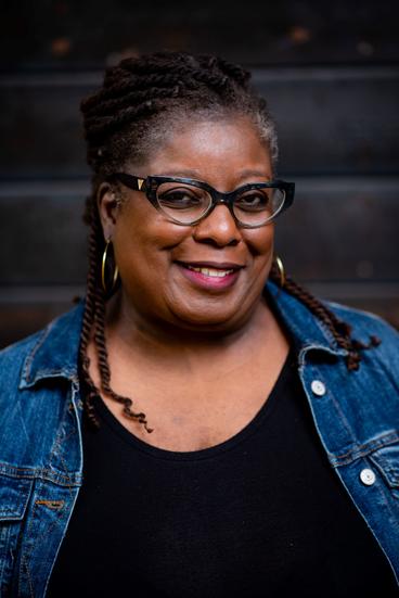 Sheryl Wilson, a black woman wearing glasses, a black shirt and jean button up.
